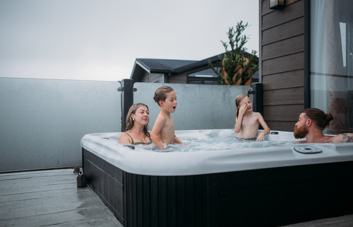 A family of four in a hot tub of a luxury lodge at Tregoad Holiday Park on a grey day