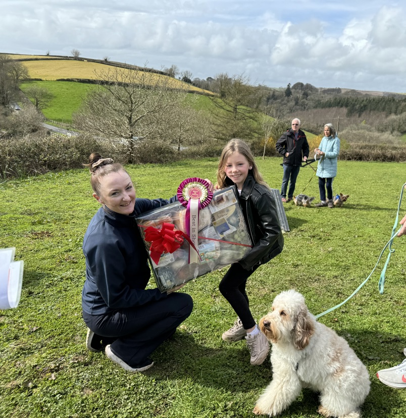 A child being presented an award for their dog at Trufts dog show at the agility course at Tregoad Holiday Park. The dog and another older man and the woman presenting the award are also in shot