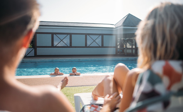 Children in pool leaning on the edge looking back at their parents who are watching them from their sun-loungers