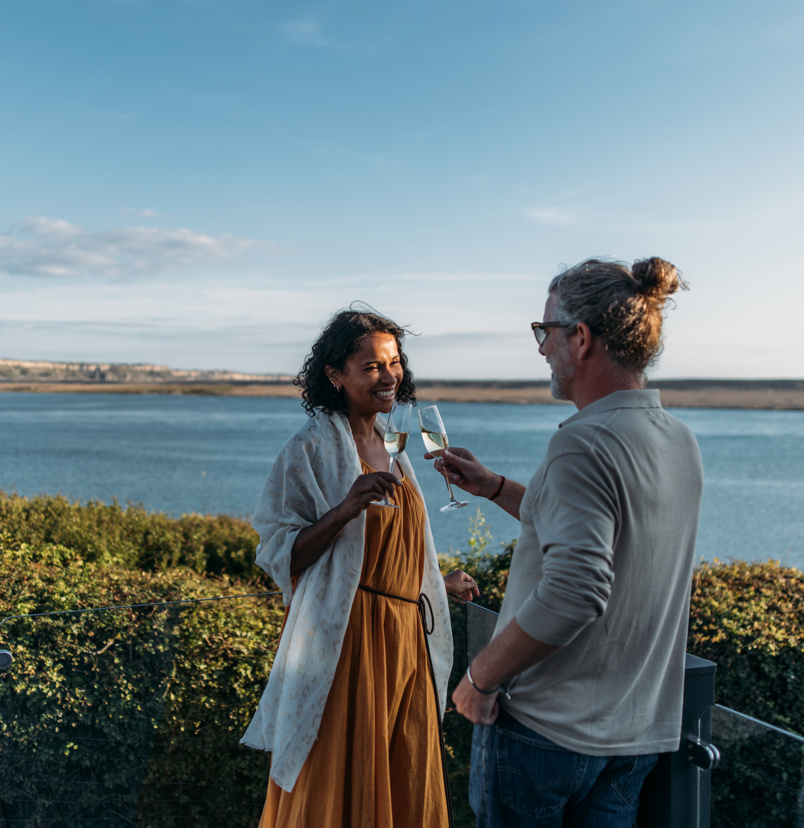 Couple celebrating with bubbly on their deck looking over chesil beach