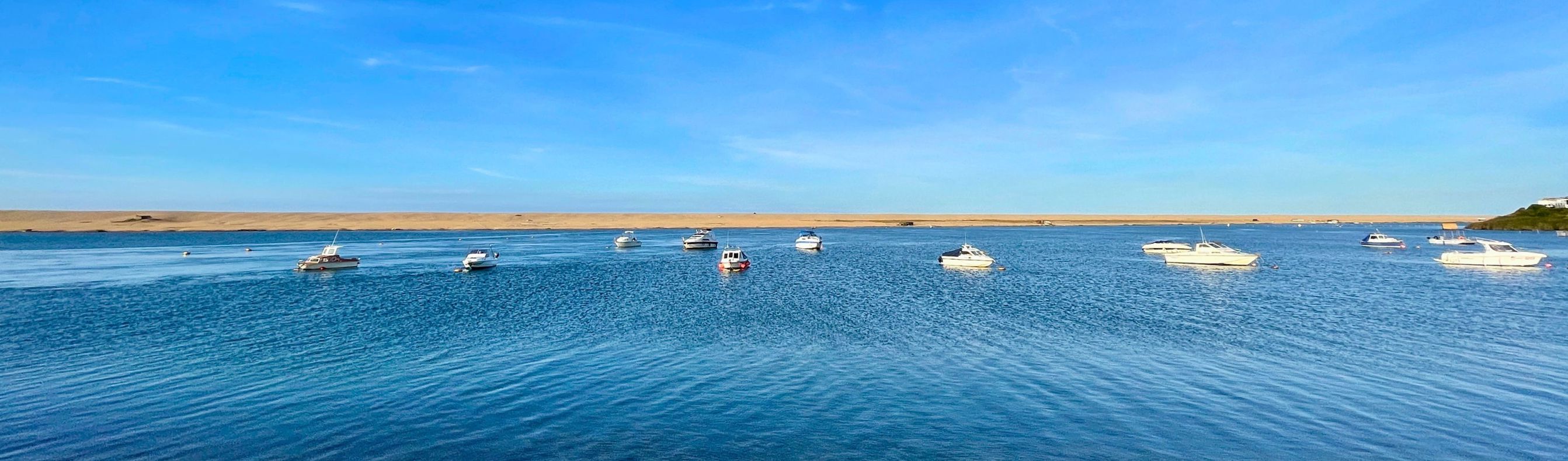 A range of boats on the sea with Chesil Beach in the background