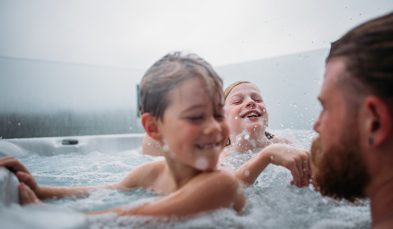 Two young boys playing in a hot tub with their dad on a cloudy day