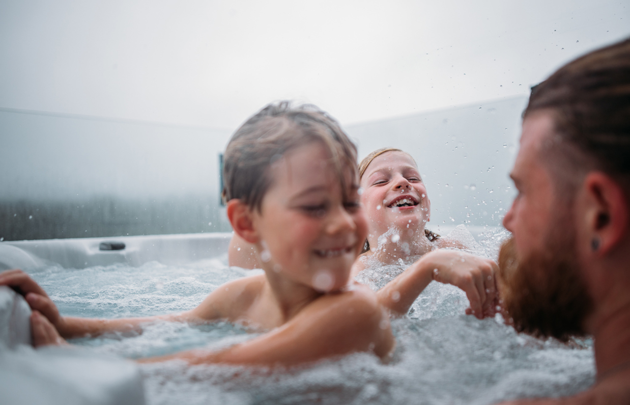 Two young boys playing in a hot tub with their dad on a cloudy day