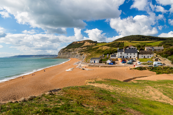 A sandy beach with blue seas, houses and hills in the background