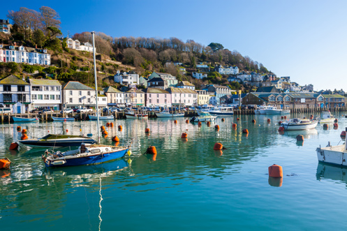 A harbour with various small boats, hills and houses on a sunny blue sky day