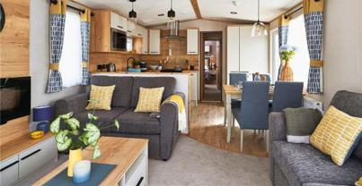 Lounge with fireplace, coffee table, and comfy grey sofas with yellow accents, looking through to kitchen and dining area