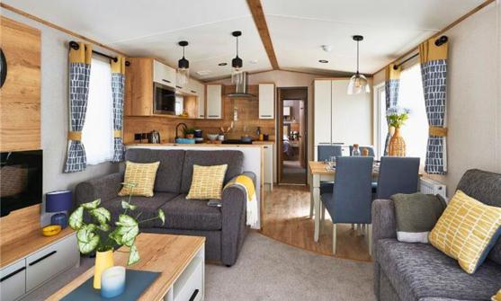 Lounge with fireplace, coffee table, and comfy grey sofas with yellow accents, looking through to kitchen and dining area