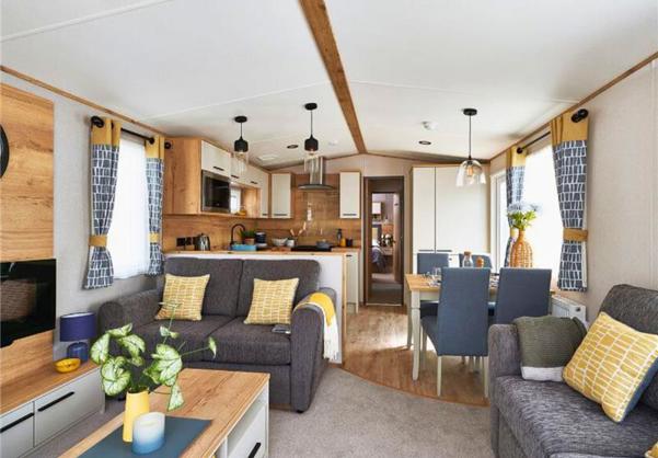 Lounge with fireplace, coffee table, and comfy grey sofas with yellow accents, looking through to kitchen and dining area
