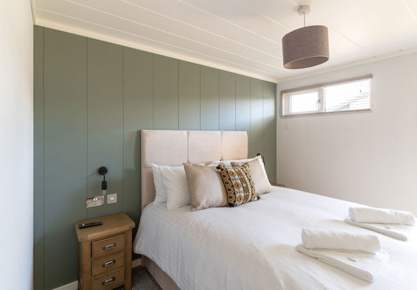 Double bedroom with sage green feature wall and comfy furnishings