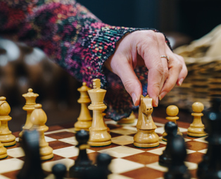 A chess board set up for play with a lady's hand reaching to move a piece