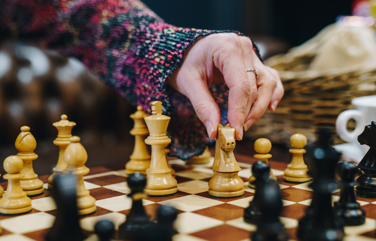 A chess board set up for play with a lady's hand reaching to move a piece