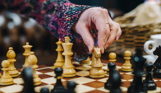 A chess board set up for play with a lady's hand reaching to move a piece