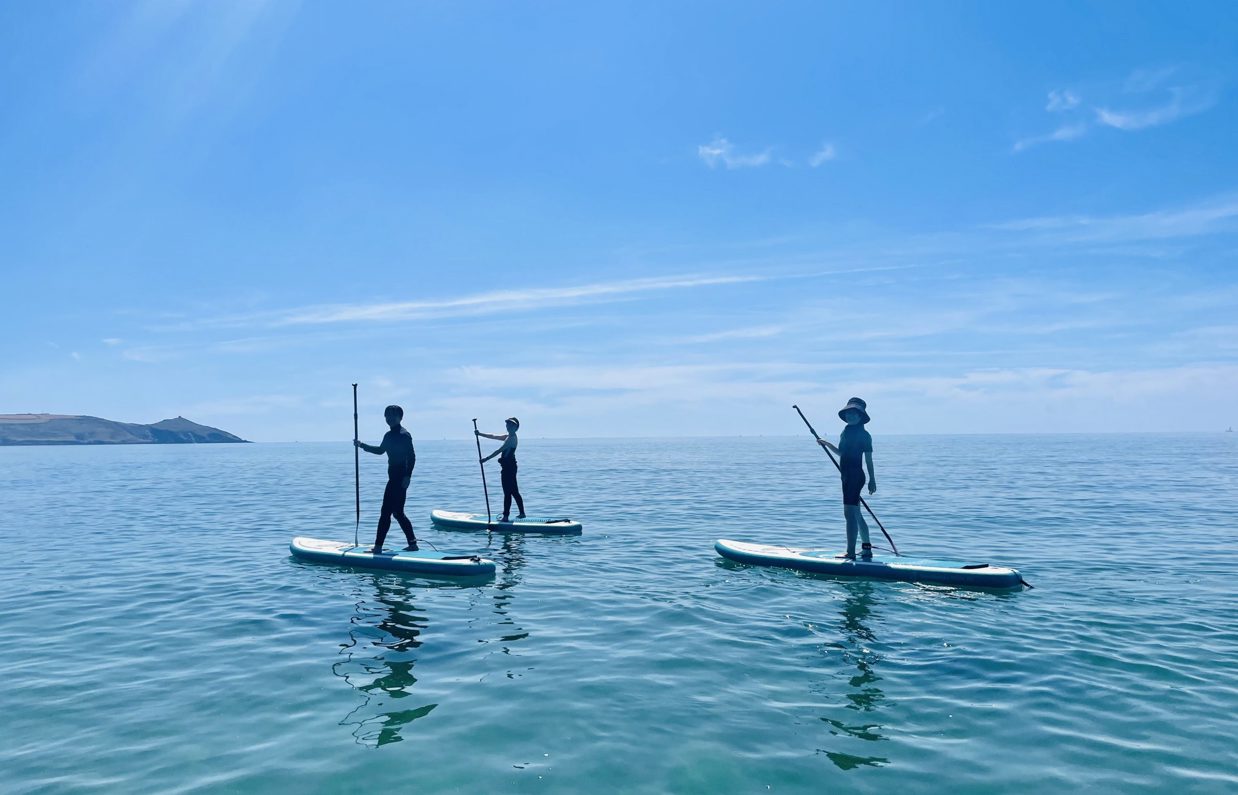 Three people standing on paddleboards in the sea on a sunny, blue sky day