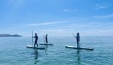 Three people standing on paddleboards in the sea on a sunny, blue sky day