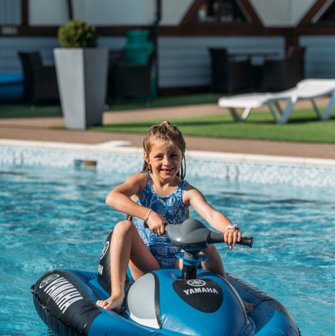 A young girl on a mini jet ski on an outdoor swimming pool