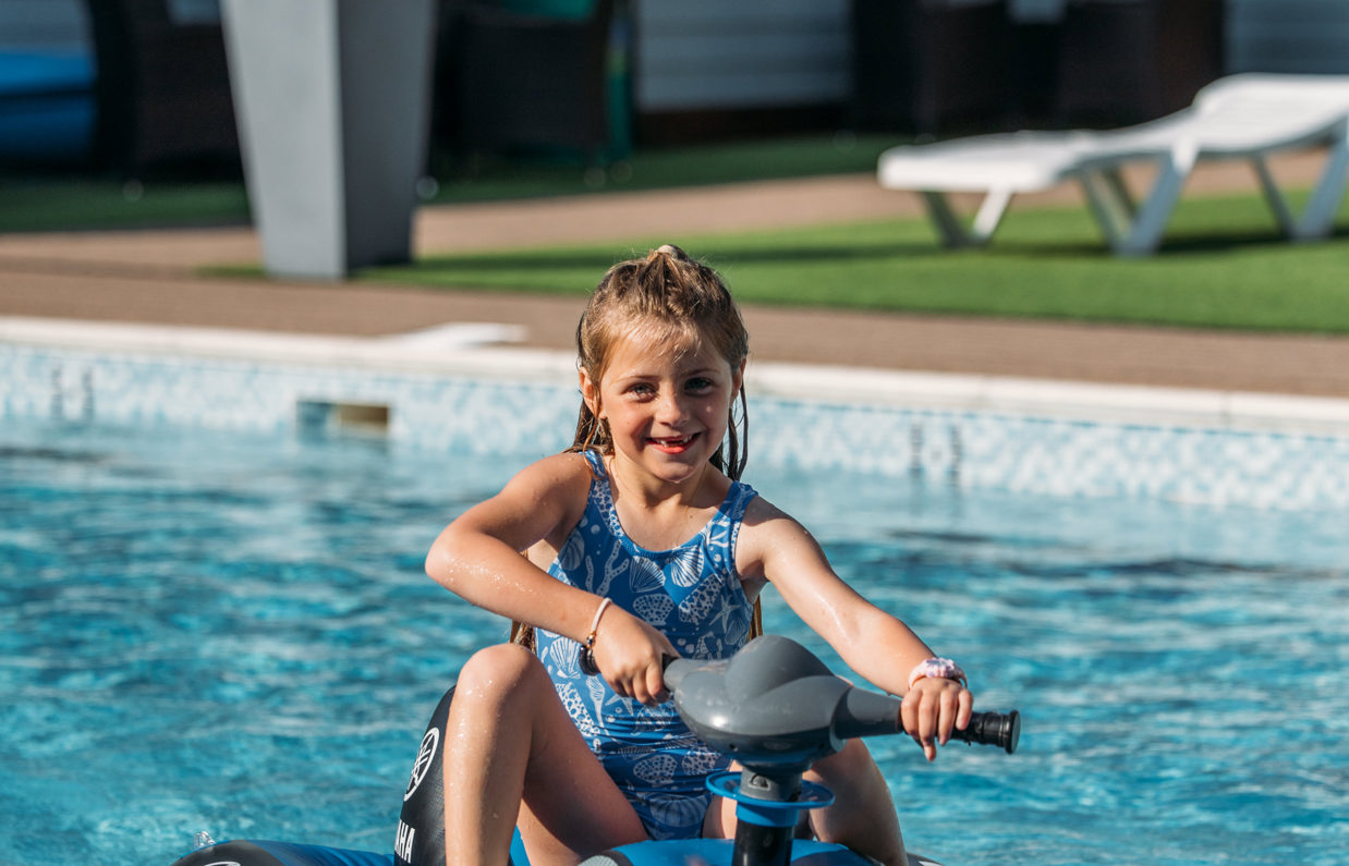 A young girl on a mini jet ski on an outdoor swimming pool