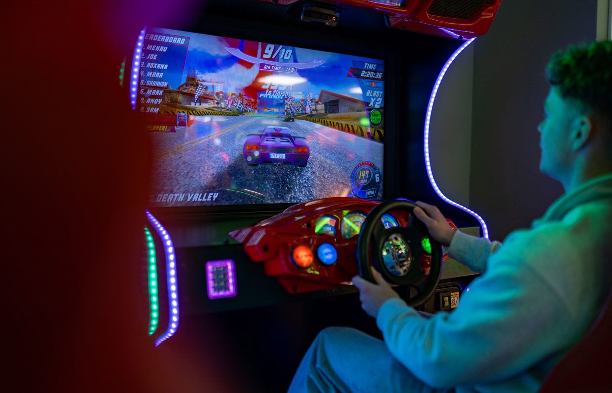 A young man sat playing an arcade car racing game