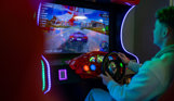 A young man sat playing an arcade car racing game