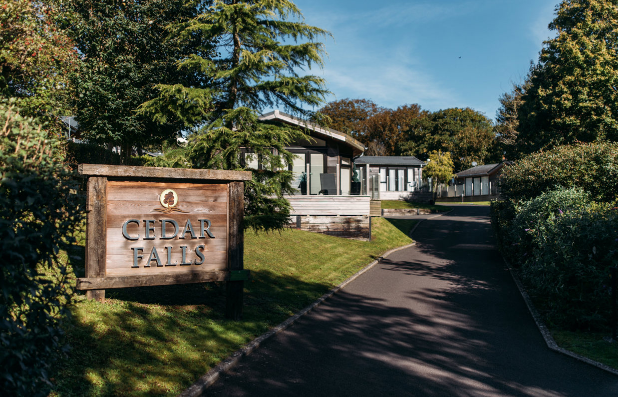Cedar Falls entrance sign on Osmington Mills Lodge Park surrounded by lodges and woodland