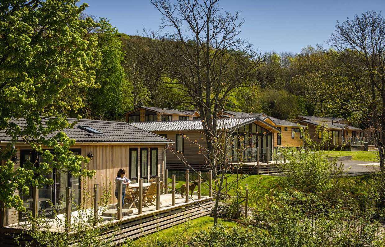 Holiday lodges among woodland and rolling countryside hills on a sunny, blue sky day