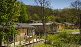 Holiday lodges among woodland and rolling countryside hills on a sunny, blue sky day