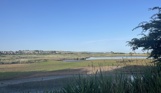 A nature reserve of wetland with cliffs, hills and houses in the background on a sunny, blue sky day