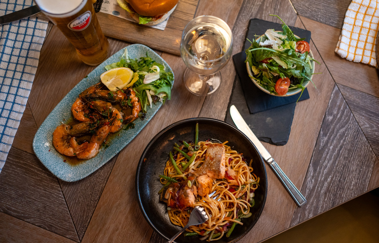 Plates of food taken from above including drinks, salmon noodle bowl, prawns and salad