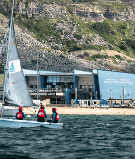 A sailing academy by the cliff side with a sailing boat in the blue water