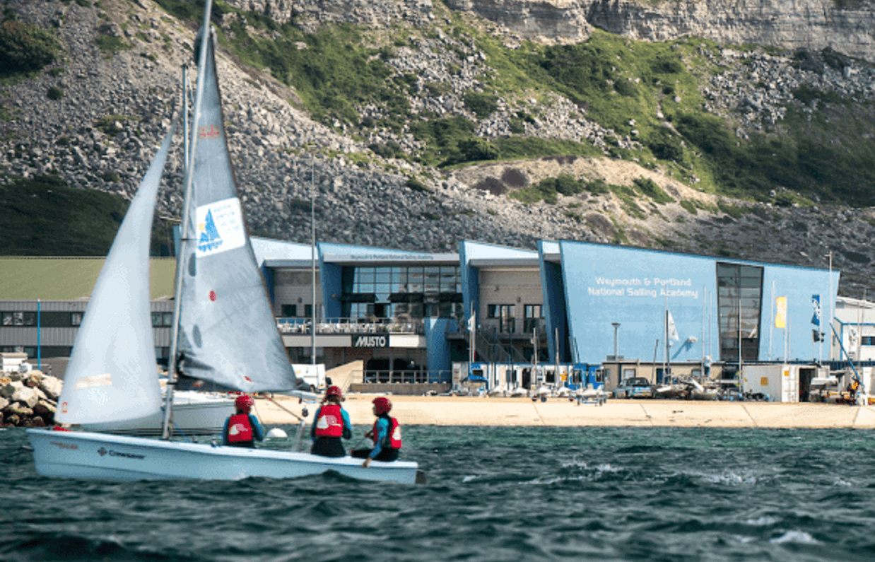 A sailing academy by the cliff side with a sailing boat in the blue water