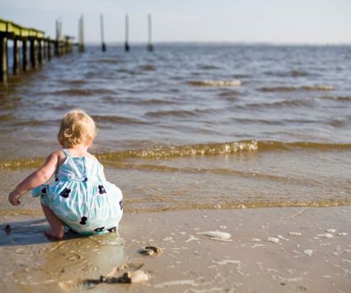 A toddler on the beach by the water