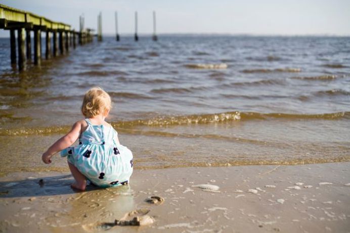 A toddler on the beach by the water