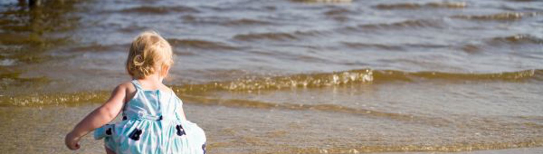 A toddler on the beach by the water