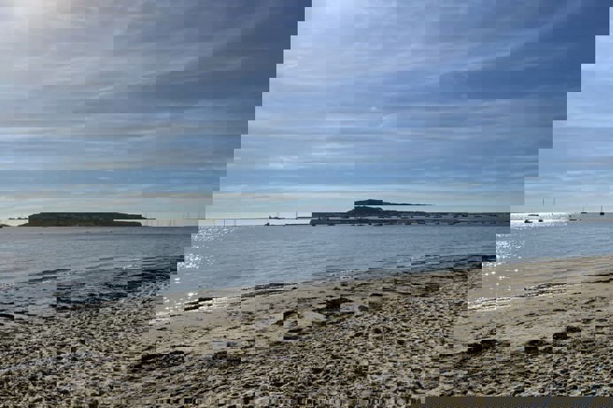 A calm sandy beach with boats in the water and blue sky