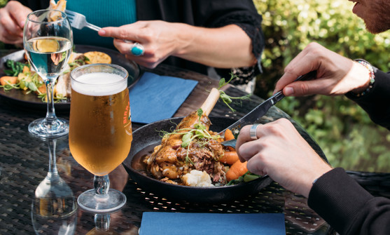 Two people sat outside eating hearty food dishes with a white wine and a pint of beer