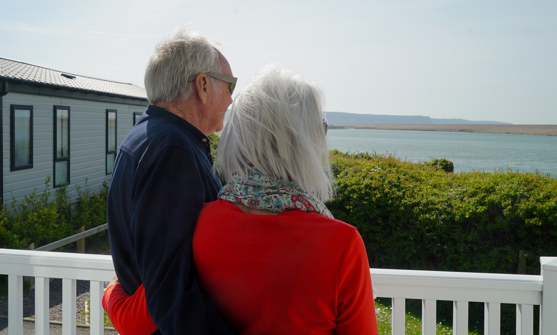 Chesil Beach Owners arm in arm on deck looking out to lagoon