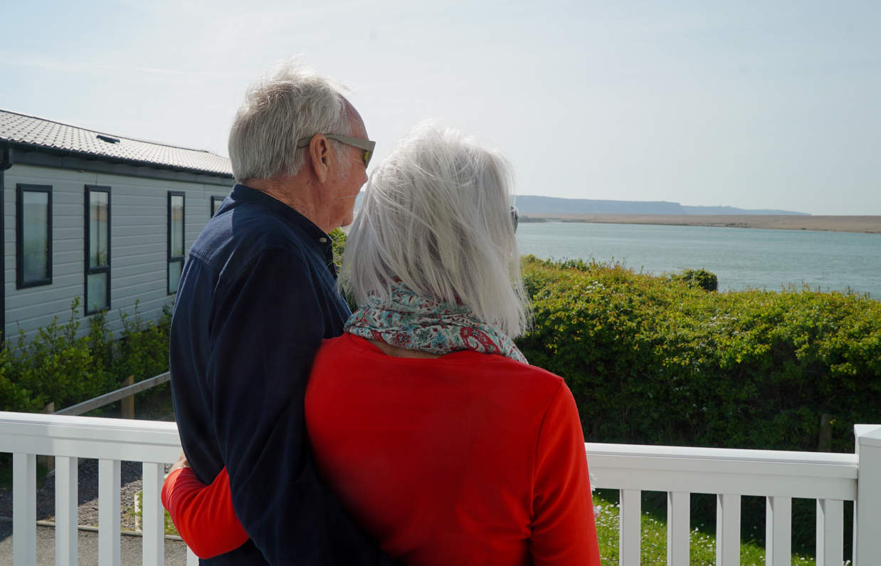 Chesil Beach Owners arm in arm on deck looking out to lagoon