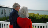 Chesil Beach Owners arm in arm on deck looking out to lagoon