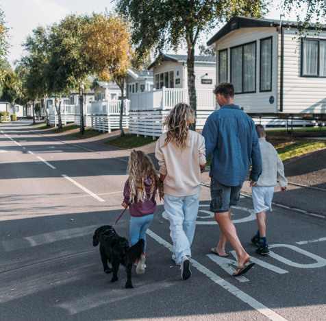 Family walking dog down a tidy lane surrounded by caravans