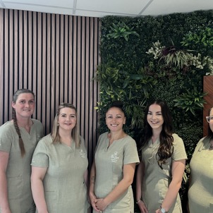 A group of ladies smiling in spa uniform against a greenery / walnut decór background