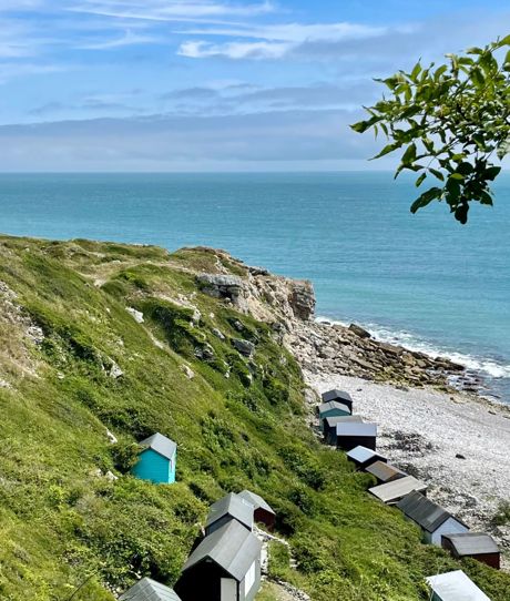 A cove with blue water down a rocky hill with various beach huts scattered