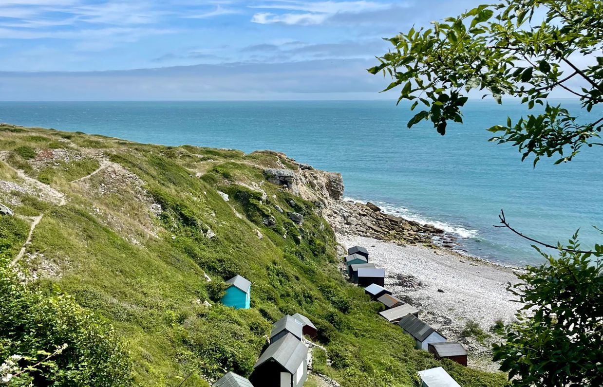 A cove with blue water down a rocky hill with various beach huts scattered