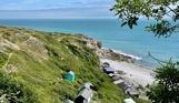 A cove with blue water down a rocky hill with various beach huts scattered