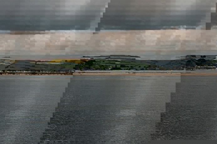 A long stretch of beach as seen from sea with rolling countryside hills in the background