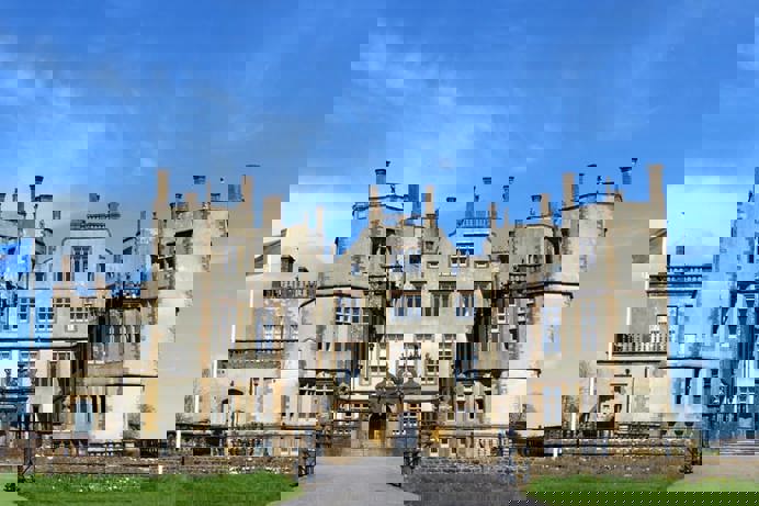 A grand looking stately home castle with grass at the front and blue sky