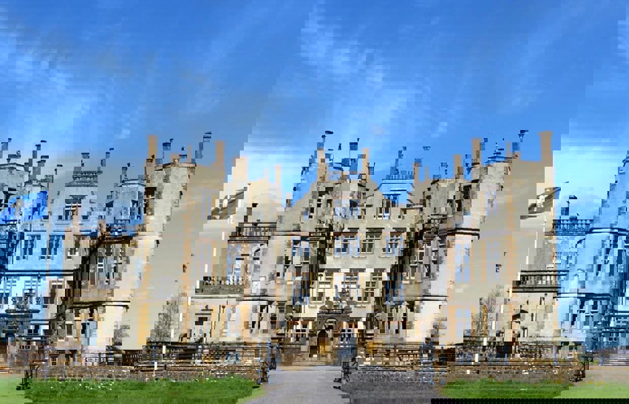 A grand looking stately home castle with grass at the front and blue sky