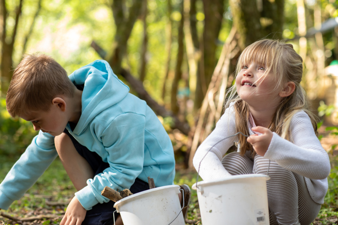 Two children among woodland foraging with buckets
