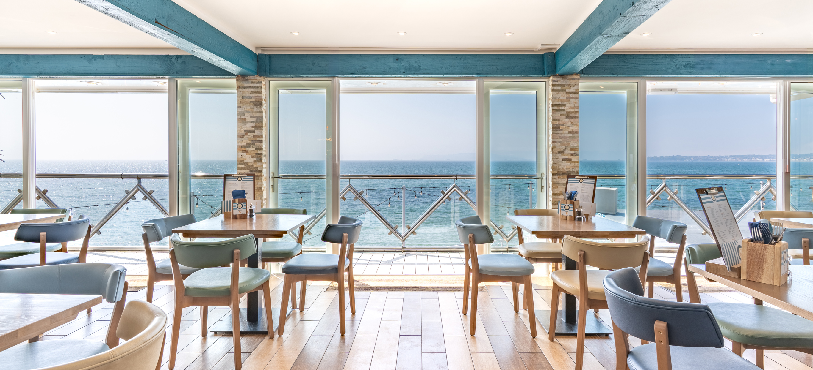 Striking sea views from the inside of Drift Bar & Grill seating area on a sunny, blue sky day