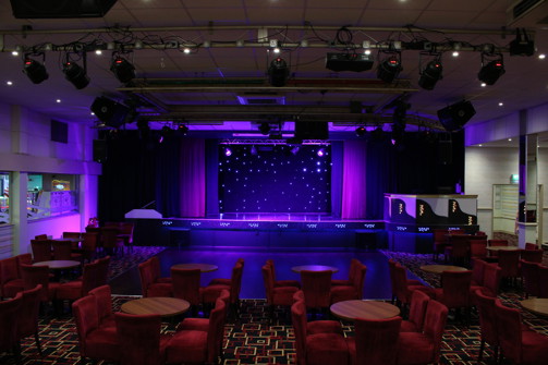 The inside of an entertainment venue with a stage and chairs and tables