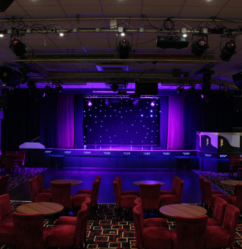 The inside of an entertainment venue with a stage and chairs and tables