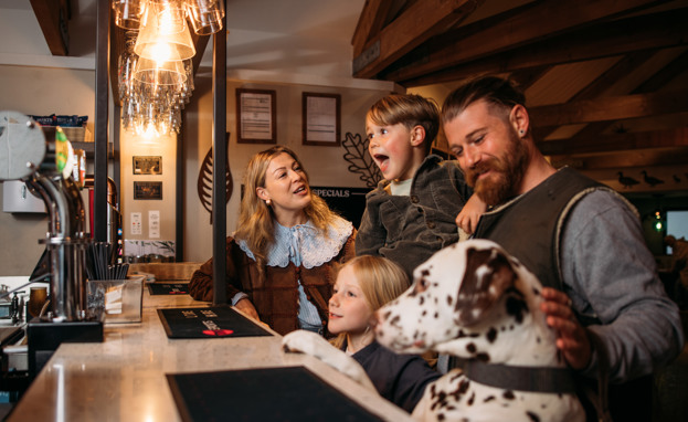 Dog with paws on bar while family order drinks